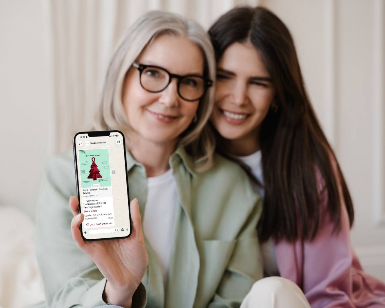 Zwei Damen lächeln und zeigen ein Handy mit Newsletter-Nachricht